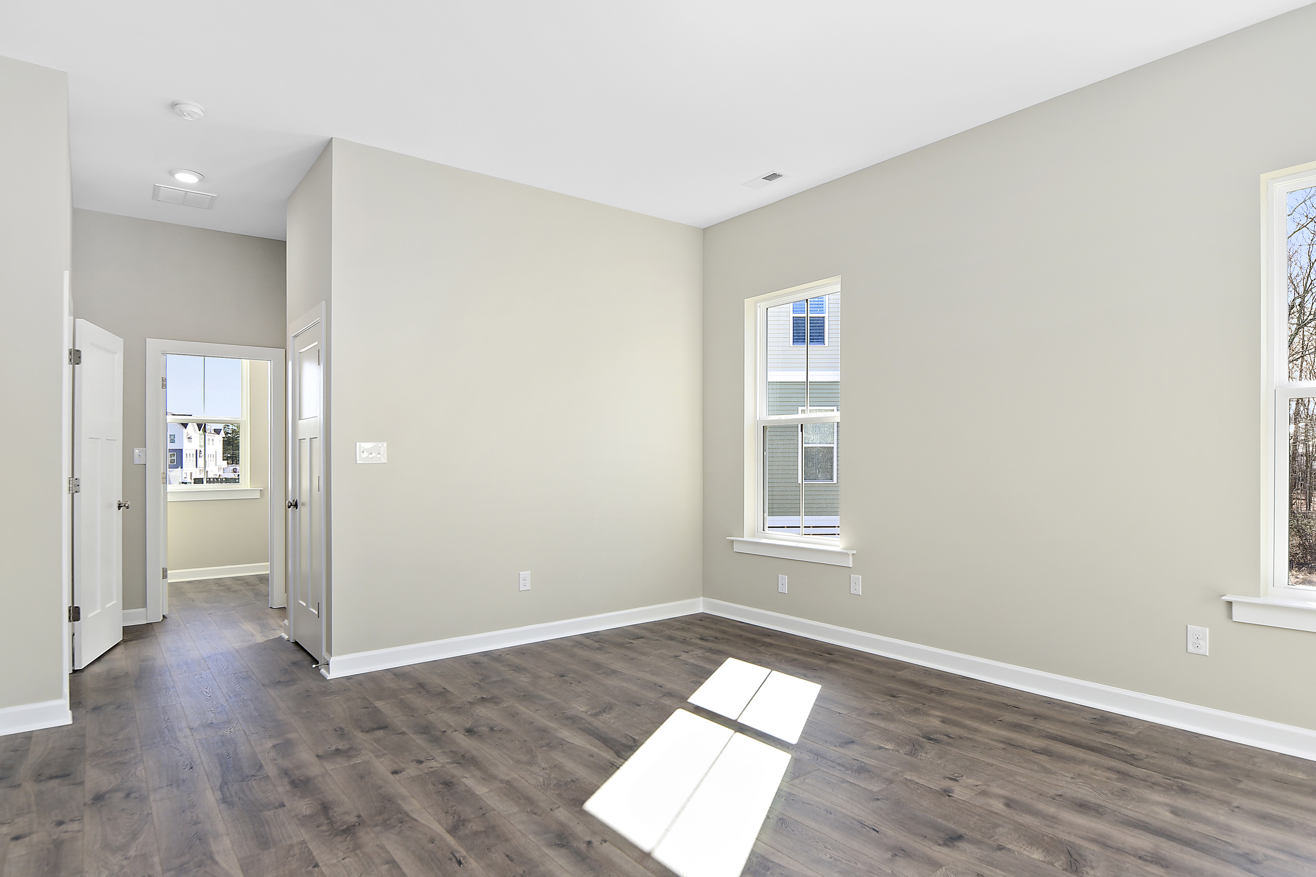Naturally lit bedroom with beige walls and hardwood flooring in Evergreene Homes new construction home