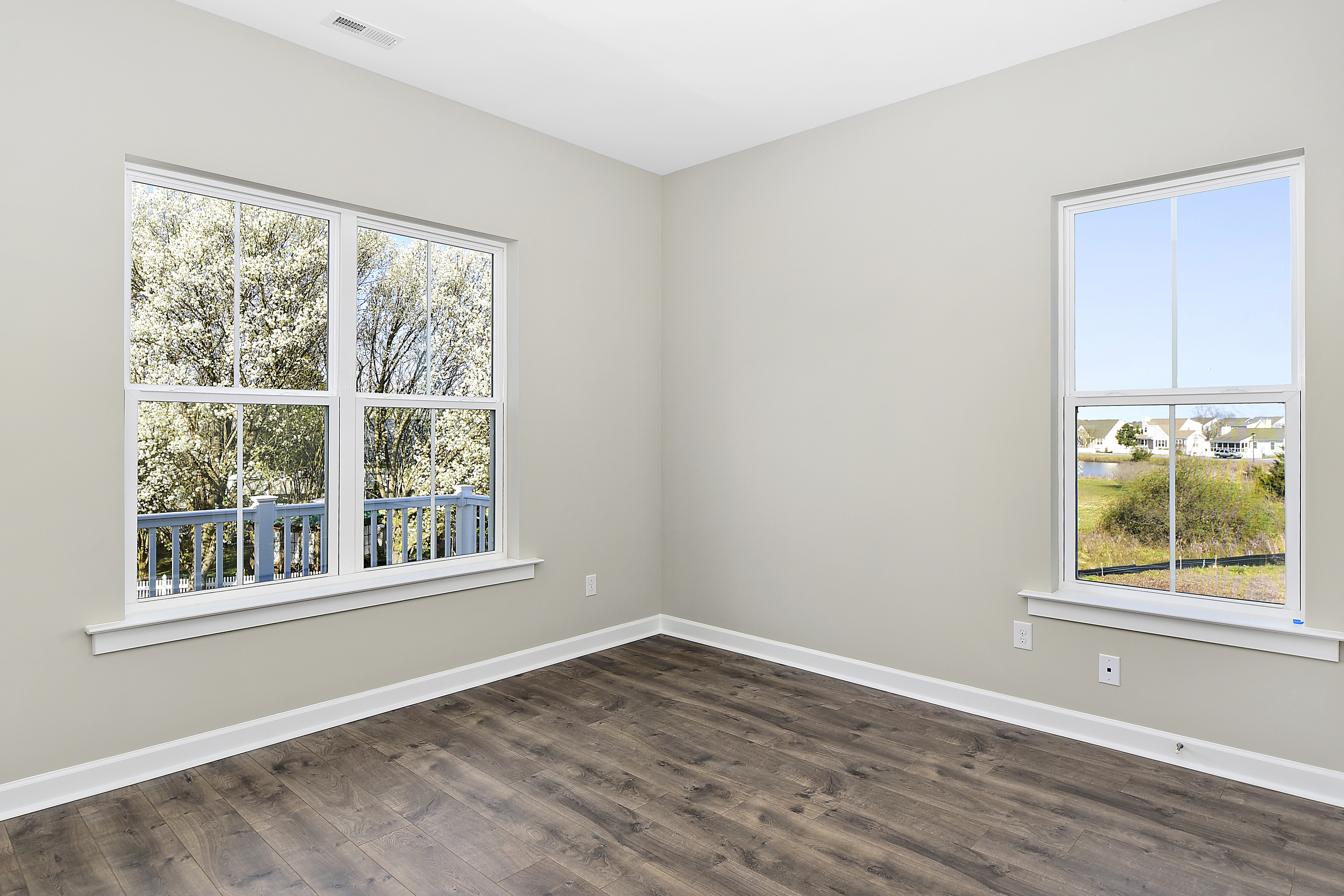 Bedroom with 2 windows, tan walls and dark hardwood flooring