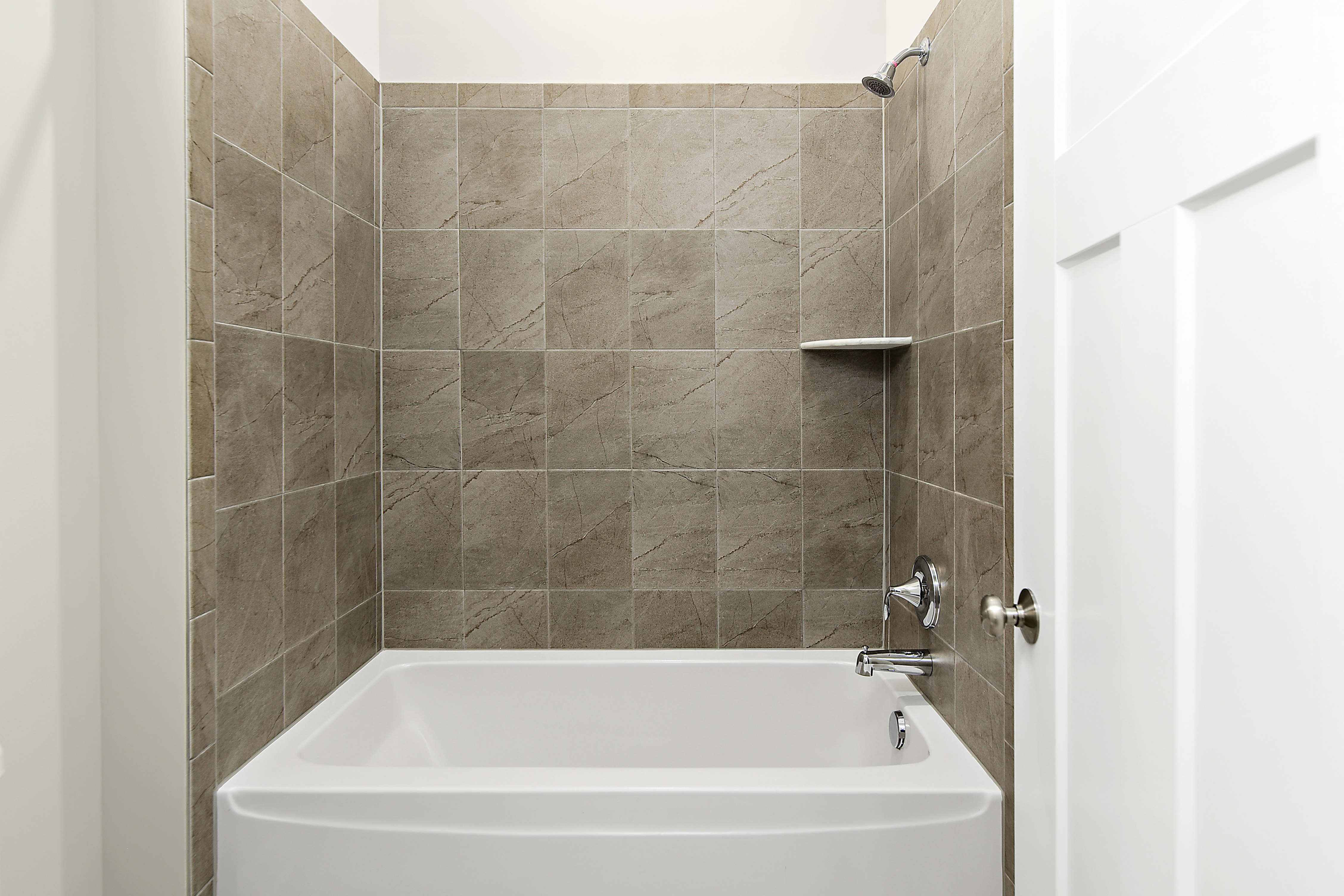 Combined shower and bathtub in bathroom of Turnstone floorplan, with white bathtub and grey brown tiles